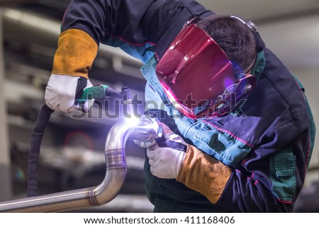Industrial worker with protective mask welding inox elements in steel structures manufacture workshop.