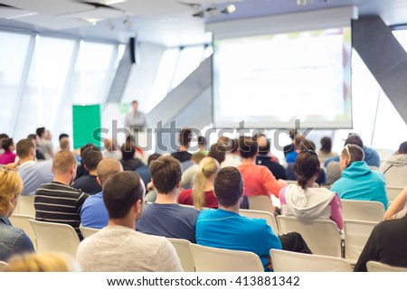 Man giving presentation in lecture hall. Male speeker having talk at public event. Participants listening to lecture. Rear view, focus on people in audience.