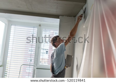 Thirty years old manual worker with wall plastering tools renovating house. Plasterer renovating indoor walls and ceilings with float and plaster. Wall mash installation. Construction finishing works.