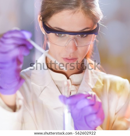 Life scientists researching in laboratory. Focused female life science professional pipetting solution into the glass cuvette. Lens focus on researcher\'s eyes. Healthcare and biotechnology concept.