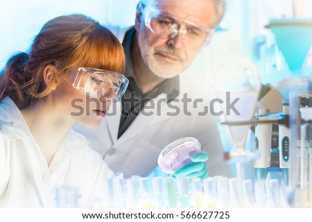Attractive young female scientist and her senior male supervisor looking at the cell colony grown in the petri dish in the life science research laboratory
