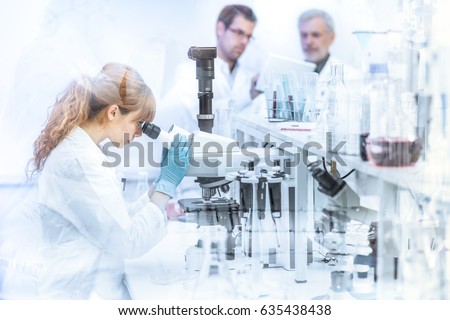 Health care researchers working in life science laboratory. Female researcher microscoping, scientists looking focused at tablet computer screen evaluating and analyzing study data.