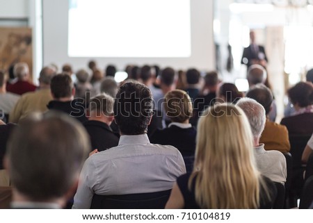 Speaker giving a talk in conference hall at business event. Audience at the conference hall. Business and Entrepreneurship concept. Focus on unrecognizable man in the audience.