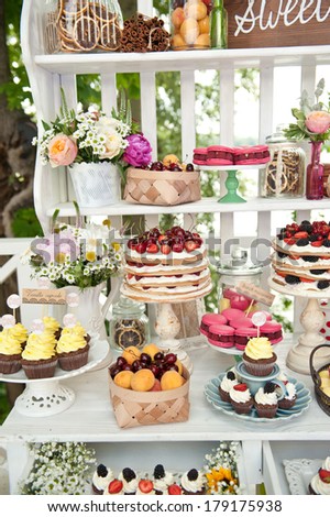 Sweet bar on summer wedding. Layer cakes with protein cream and fresh cherry and berries on a cake stand outdoors