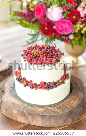 Cake with protein cream and fresh berries on a wooden cake stand outdoor