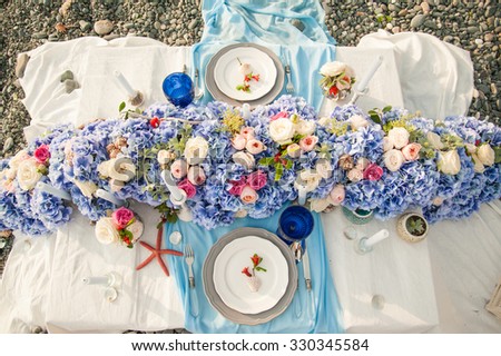 Elegant wedding reception area for bride and groom, ready for the bridal party. Rich bunch of flowers table. Sea concept.