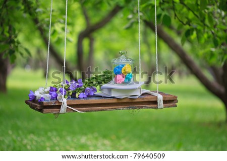 Still life - books, summer flowers and  a glass jar with colorful baby\'s dummy on a swing outdoors