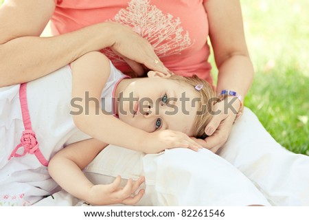 Young girl with blonde hair, white dress lying on her Grandmother legs and embraced by her arms.