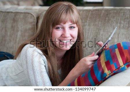 Close up of smiling blond teen reading e-reader on the couch