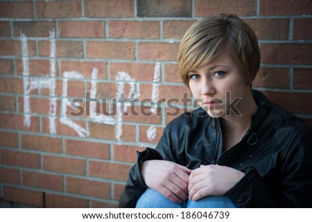 Depressed, sad teen girl sits outside school wall, asking for help