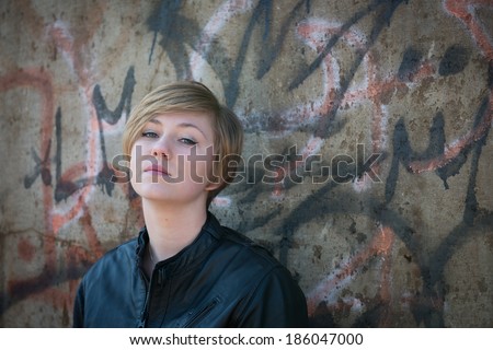 Depressed teen girl in leather jacket, with graffiti wall as background