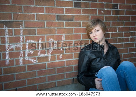 Sad, depressed girl outside school, with red brick background