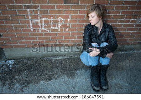 Sad, depressed girl outside school, with red brick background