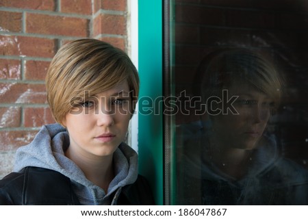 Sad teen girl outside school, with reflection from door window