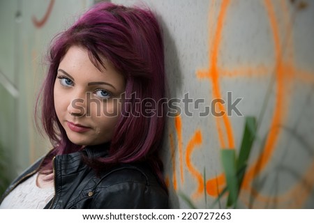 Sad teen girl leans up against graffiti covered wall outside school
