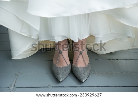 Bride's shoes under white wedding dress, on rustic wooden floor