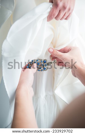 Something old, something new, something borrowed, something blue: Maid of honor pins antique brooch with blue gems on on bride's dress