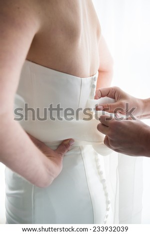 Brides maid helps bride dress in wedding dress for wedding day