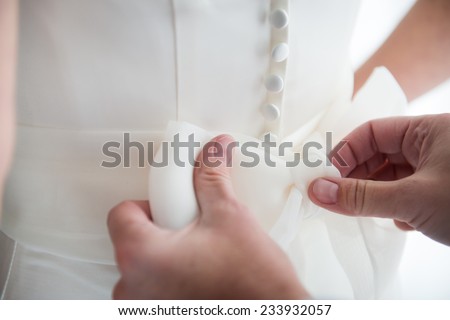 Brides maid helps bride dress in wedding dress for wedding day