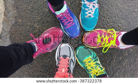Overhead view of 6 brighlty colored runners\' shoes on wet pavement