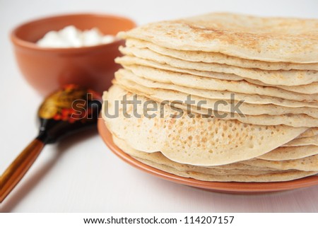 Stack of pancakes on ceramic plate, sour cream, painted wooden spoon