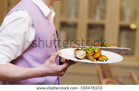 Waiter carrying two plate with meat and baked potato