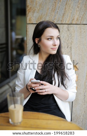 Young woman drinking ice coffee and using her mobile phone in a outdoor cafe