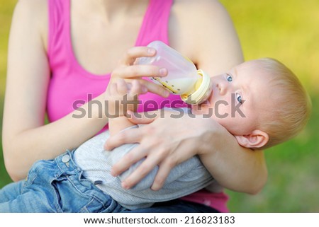 Adorable baby boy drinking milk from bottle in mother hands