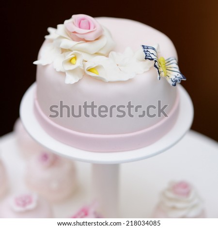 Delicious pink wedding cake and cupcakes decorated with flowers and butterfly