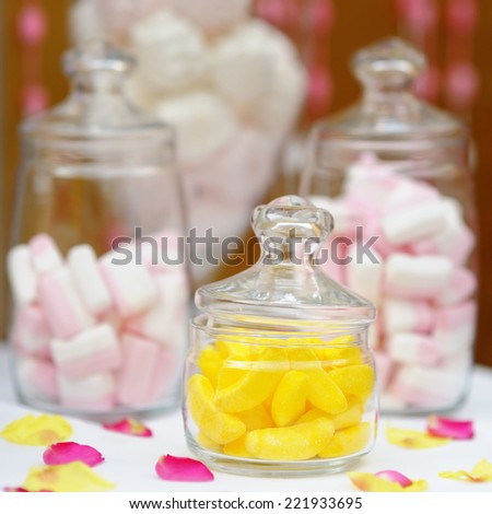 Yellow fruit candy and marshmallow in glass jars on sweet table or candy bar
