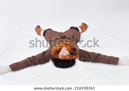 Winter fun - snow angel - young beautiful woman playing in snow
