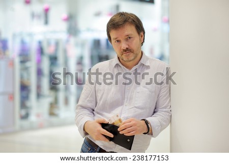 Stressed middle age man holding purse with russian paper money (rubles) at shopping mall