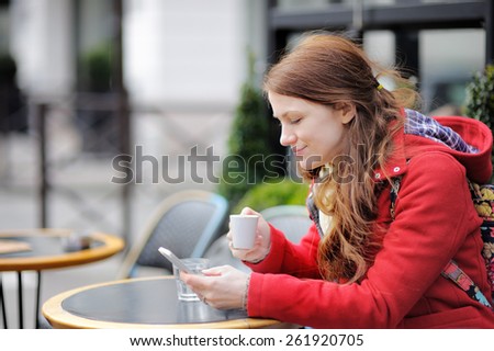 Young woman drinking coffee and using her smart phone in a Parisian street cafe