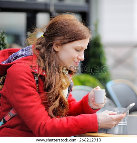 Young woman drinking coffee and using her smart phone in a Parisian street cafe