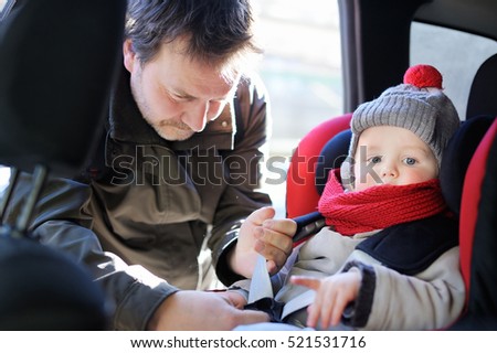 Middle age father helps his toddler son to fasten belt on car seat