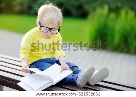 Cute toddler boy reading a book outdoors on warm summer day. Back to school concept