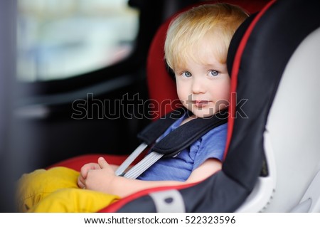 Portrait of cute toddler boy sitting in car seat. Child transportation safety