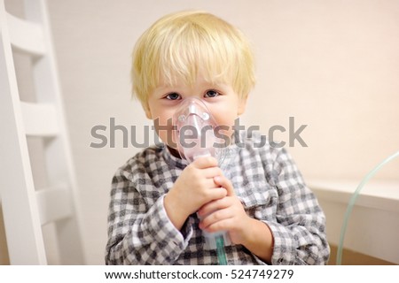 Cute boy inhalation therapy by the mask of inhaler. Close up image of a little kid with respiratory problem or asthma. Sick boy with clear oxygen mask.