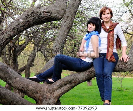 Attractive woman and her grown-up daughter sitting on a tree