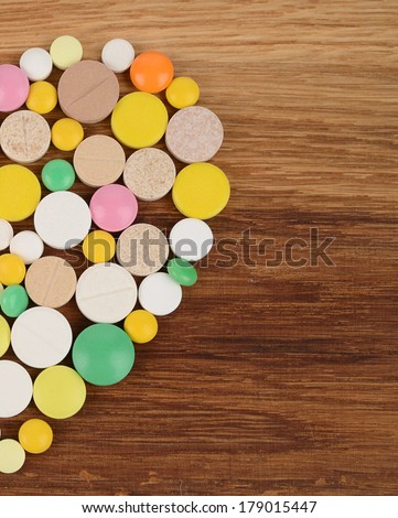 Half a heart of different pills on a wooden background