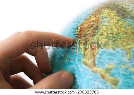 Hand touching globe on white background. The globe is marked with a black line, possibly planning a coast to coast journey from New York to Los Angeles. The west coast is in focus.