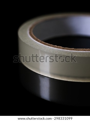 Close up shot of sticky tape roll on reflective black background.