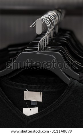 A selection of black V-neck shirts hanging on a clothes rail by coat hangers. The identical shirts are all new with labels attached.