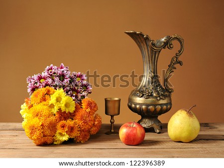 Metal jug, flowers and fruits on the table