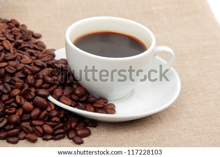 Textured background of dark brown roasted coffee beans background and cup of coffee on Food and Drink conceptual theme