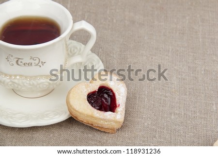 Top view of stylish ivory tea cup with heart-shaped biscuit with sweet jam inside on tea time on Sign and Symbol theme
