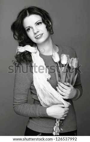 Studio black and white image of beautiful young girl with a bouquet of spring flowers