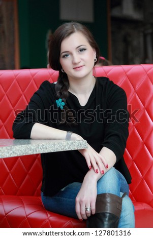 Pretty brunette sitting on a red sofa in cafe
