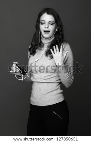 Black and white photo of emotional pretty girl  with telephone listening to music and dancing