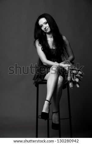 Portrait of a sexy brunette in a short black dress sitting on a stool with a bouquet of flowers
